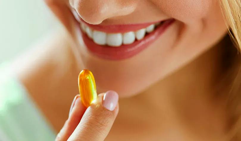Une femme tient une pilule de vitamines à la main.