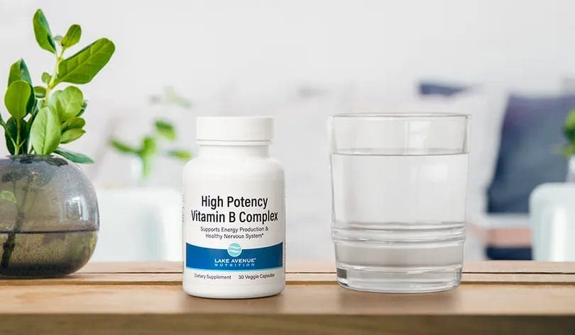 Une bouteille de vitamines et de suppléments très puissants sur une table à côté d'un verre d'eau.